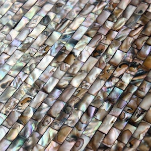 Op de afbeelding: Close-up van een mozaïektegelpatroon. De rechthoekige tegels zijn diagonaal gerangschikt, waardoor een textuur ontstaat. De tegels hebben iriserende kleuren, waaronder bruin, wit en hints van blauw en groen, met een parelmoereffect.