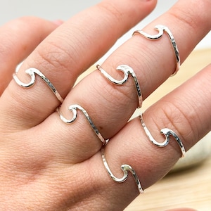 May include: Five silver wave rings stacked on a finger. The rings are hammered and have a textured finish.