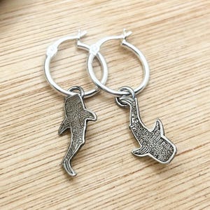 Könnte beinhalten: Silberne Creolen mit einem Hai-Anhänger.