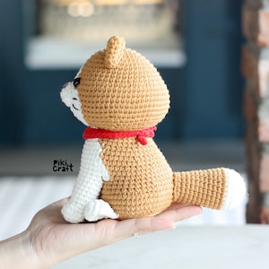 May include: A crocheted tan and white dog with a red collar. The dog is sitting on a hand.