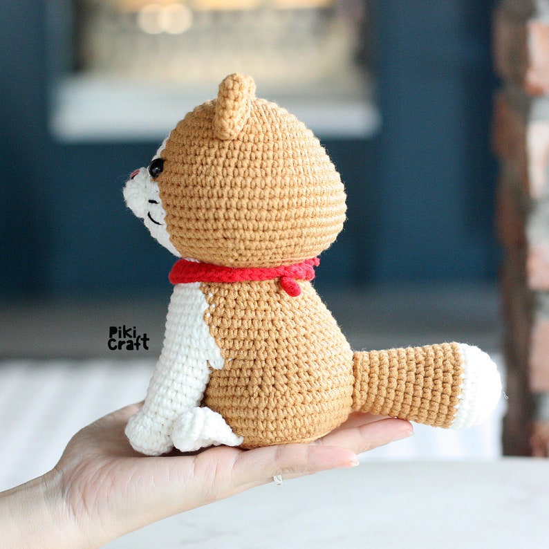 May include: A crocheted tan and white dog with a red collar. The dog is sitting on a hand.