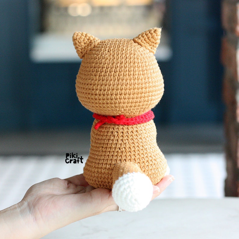 May include: A crocheted brown and white dog with a red bandana. The dog is sitting on a hand.