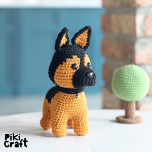 K&ouml;nnte beinhalten: Ein geh&auml;keltes Stofftier in Form eines Deutschen Sch&auml;ferhundes. Der Hund ist braun und schwarz mit einer goldenen Glocke am Halsband.