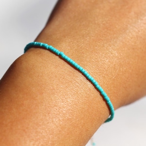 Peut inclure: Un bracelet en perles turquoise porté au poignet. Le bracelet est composé de petites perles rondes enfilées sur un cordon fin.