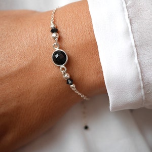 May include: A silver chain bracelet with a black gemstone and black beads.