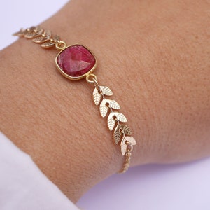Peut inclure: Un bracelet en or avec une pierre précieuse rouge et un motif de feuilles.