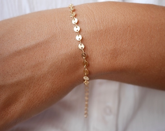 May include: A gold chain bracelet with small, round, flat links. The bracelet is on a person's wrist.