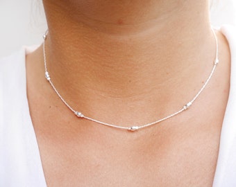 May include: A delicate silver necklace with small, evenly spaced beads. The necklace is thin and has a simple design.