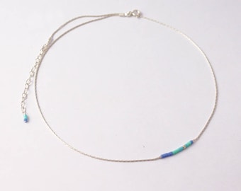 May include: A silver chain necklace with a blue and green beaded accent.