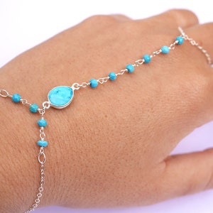 May include: A turquoise and silver chain bracelet with a large turquoise gemstone. The bracelet is designed to be worn on the wrist and finger.