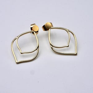 May include: A pair of gold-colored leaf-shaped earrings. Each earring features a double-layered design with a post backing. The earrings are displayed on a white surface, showcasing their minimalist and elegant style.