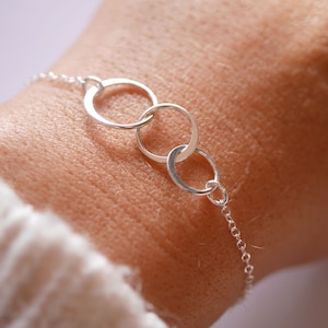 Peut inclure: Un bracelet en argent avec trois cercles entrelacés. Le bracelet est porté au poignet.
