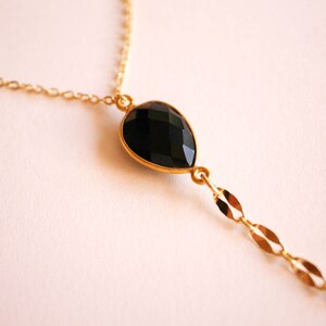 May include: A gold chain necklace with a black gemstone pendant. The pendant is a teardrop shape and has a faceted cut.