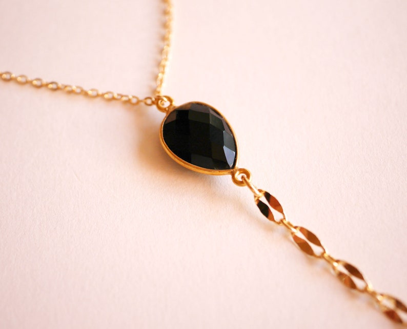 May include: A gold chain necklace with a black gemstone pendant. The pendant is a teardrop shape and has a faceted cut.