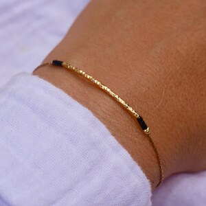 Puede incluir: Un brazalete de oro con una barra texturizada y detalles de cuerda negra.
