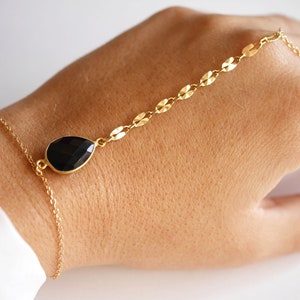 May include: A gold chain bracelet with a black teardrop-shaped gemstone. The bracelet is designed to be worn around the wrist and up the arm.