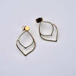 May include: A pair of gold-colored, open-frame earrings. Each earring features a double-layered, teardrop-shaped design. The earrings are displayed on a white surface, showcasing their minimalist and elegant style. The earring posts are visible.