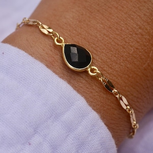 Peut inclure: Un bracelet en chaîne dorée avec une pierre précieuse noire en forme de larme.