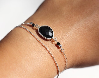 Peut inclure: Un bracelet en chaîne argent avec un pendentif en pierre noire et de petites perles noires.