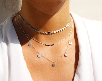 Op de afbeelding: Een gelaagde zilveren ketting met een choker-stijl bovenste laag van kleine zilveren schijven en een onderste laag met hangende zilveren schijven.