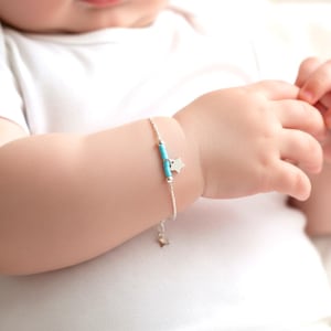 Peut inclure: Un bracelet délicat en argent avec des perles turquoise et un petit charme en forme d'étoile. Le bracelet est conçu pour un bébé ou un jeune enfant. Le bracelet est sur le poignet d'un bébé.