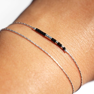 May include: Two silver bracelets on a wrist. One bracelet is a simple chain, the other has black beads.