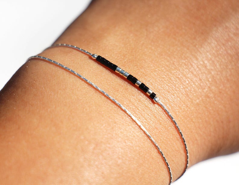 Pode incluir: Duas pulseiras prateadas em um pulso. Uma pulseira &eacute; uma corrente simples, a outra tem contas pretas.