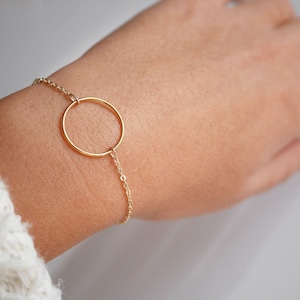 Peut inclure: Un bracelet délicat en chaîne dorée avec un pendentif rond simple.