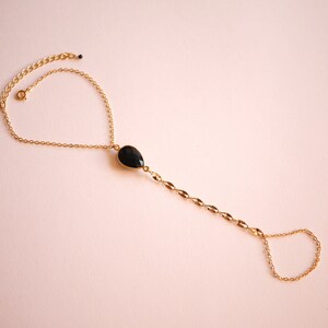 May include: A gold chain bracelet with a black gemstone pendant. The bracelet has a delicate chain and a small ring at the end for adjusting the size.