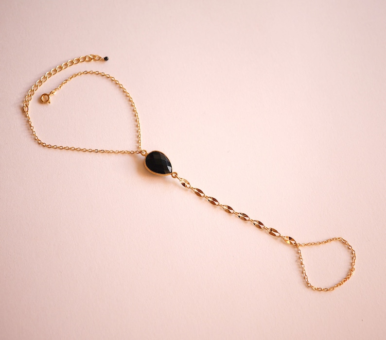 May include: A gold chain bracelet with a black gemstone pendant. The bracelet has a delicate chain and a small ring at the end for adjusting the size.