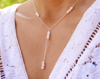 Può includere: Una collana a catena d'argento con perline bianche. La collana ha un design a forma di Y con tre perline in basso e due perline su ciascun lato della Y.