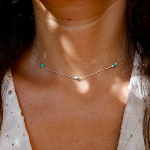May include: A delicate silver necklace with three small turquoise stones.