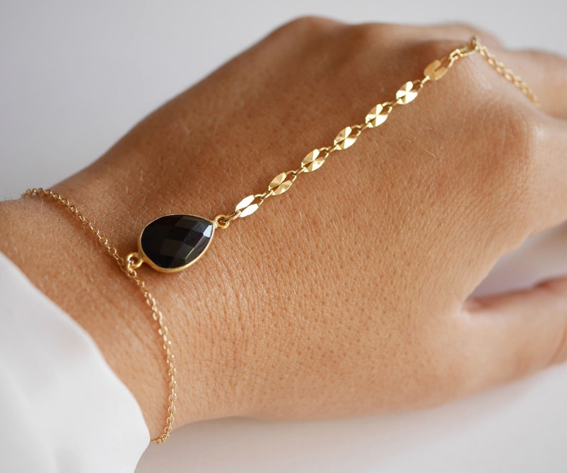 May include: A gold chain bracelet with a black teardrop-shaped gemstone. The bracelet is adjustable and has a delicate chain.