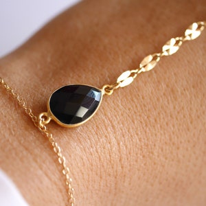 May include: A gold chain bracelet with a black teardrop-shaped gemstone pendant.