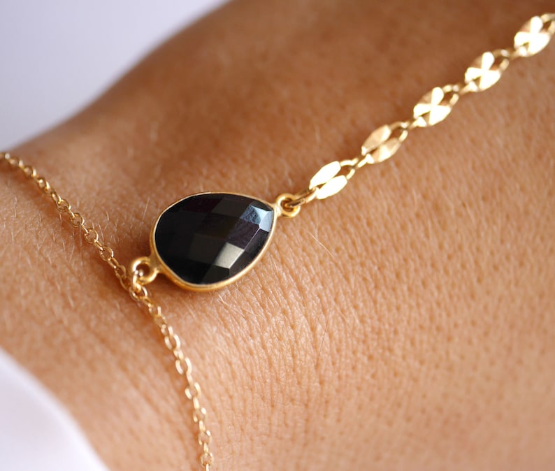 May include: A gold chain bracelet with a black teardrop-shaped gemstone pendant.