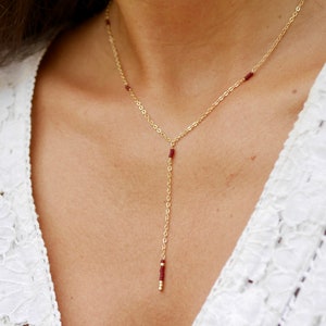 Op de afbeelding: Een gouden ketting met kleine rode kralen. De ketting is lang en heeft een Y-vormig ontwerp.
