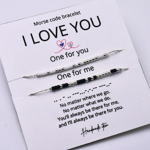 May include: Two Morse code bracelets on a white card, with the text "I LOVE YOU". One bracelet is white with silver beads, the other is black with silver beads. The card also includes the text "One for you, One for me".