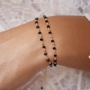 May include: A delicate gold chain bracelet with black beads. The bracelet is layered and features a simple design.