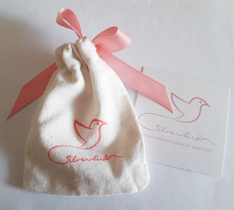 May include: A white drawstring bag with a pink ribbon and a pink bird logo. The bag is labeled "Silver Bird" and "atelier-creation bijoux en argent 925".