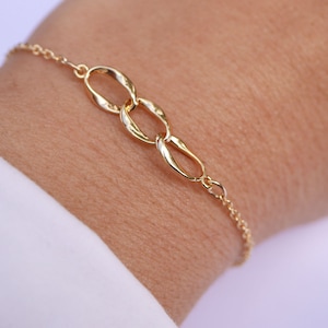 Könnte beinhalten: Ein goldenes Kettenarmband mit drei miteinander verbundenen, verdrehten, ovalen Anhängern.