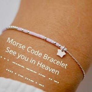 Puede incluir: Una pulsera delicada con un centro de cuentas rosadas y una cadena plateada. La pulsera presenta un pequeño dije de estrella y el texto "Morse Code Bracelet See you in Heaven". El código Morse deletrea "See you in Heaven".