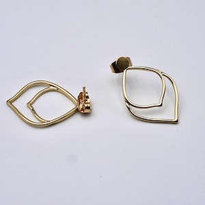 May include: A pair of gold-colored, open-frame earrings. Each earring features a double leaf design. The earrings are displayed on a white surface, showcasing their delicate, minimalist style. The earrings have post backs.