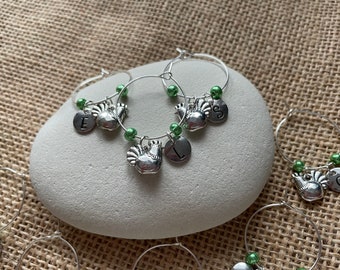 May include: Set of six silver wine glass charms with green beads and a rooster charm. Each charm has a letter on it, E, L, S, C, and two others.