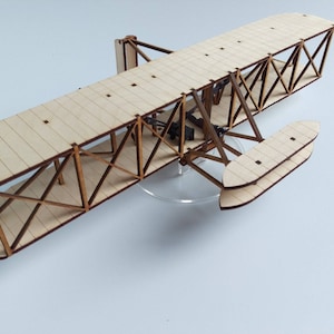 Könnte beinhalten: Ein Holzmodell des Wright Flyer, des ersten erfolgreichen Flugzeugs. Das Modell ist aus hellbraunem Holz gefertigt und hat eine Spannweite von etwa 30 cm.