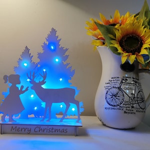 Escena de madera iluminada navideña: niña y ciervo con árboles, decoración de madera de invierno