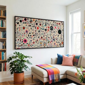 May include: A living room with a large, colorful abstract art piece in a black frame above a beige sectional sofa. A potted plant, a patterned rug, and framed art pieces add to the room's decor. Bookshelves and windows are also visible.