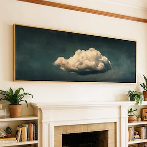 May include: A panoramic rectangular wall art piece featuring a single, fluffy white cloud centred against a dark, moody teal and charcoal sky. The artwork is enclosed in a thin, metallic gold frame and is mounted horizontally above a fireplace.