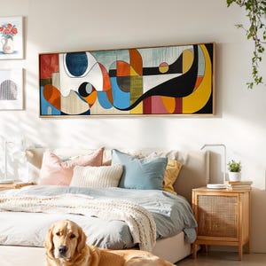Puede incluir: Una pieza de arte mural rectangular larga que presenta una composición abstracta de formas geométricas audaces y líneas fluidas en tonos azul, naranja, amarillo, negro y blanco, enmarcada en un borde de madera clara sobre una cama.