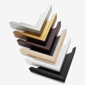 May include: A collection of picture frame corners in various colors, including silver, gold, brown, black, and white. The frames are stacked, showcasing the different wood finishes and styles. The image highlights the variety of options available for framing artwork.