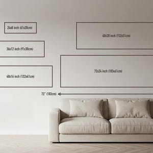 a wall with a large canvas or painting displayed on it, along with a beige sofa or couch positioned in front of it. The wall has a simple, clean design, and the size of the canvas is described in inches and centimeters.